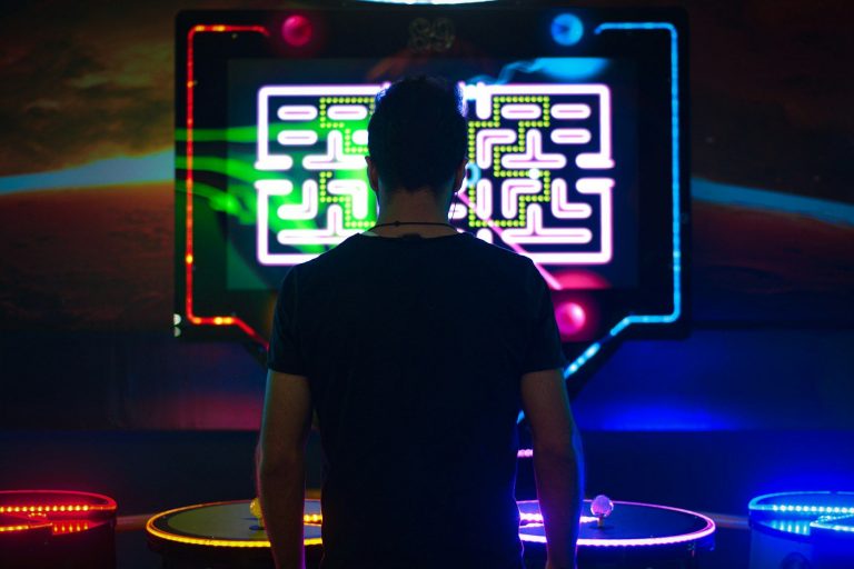 Person steht vor Joysticks und großem Bildschirm mit Pac-Man-Labyrinth und LED-Beleuchtung.